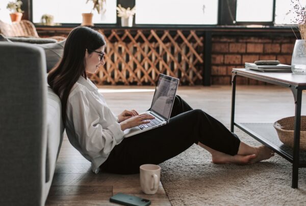 kobieta z laptopem na kolanach siedząca na podłodze w salonie - poszukiwanie pracy - KZ Inspire