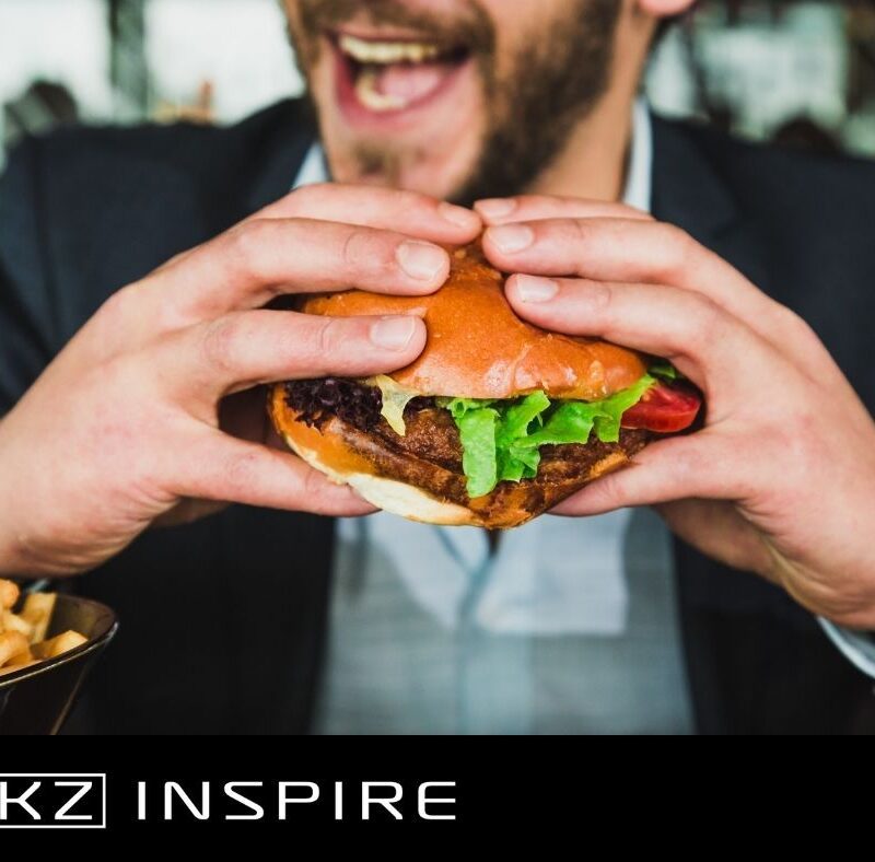 mężczyzna trzymający hamburgera w dłoniach - jak wspierać organizm w pracy - KZ Inspire